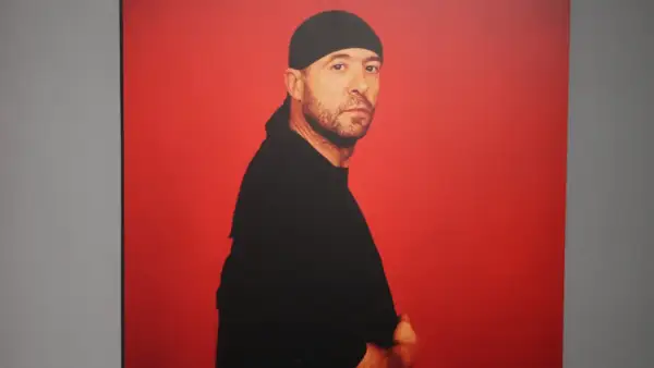 Retrato de Manuel Piña con gorro y camiseta negra, sobre fondo rojo vibrante.