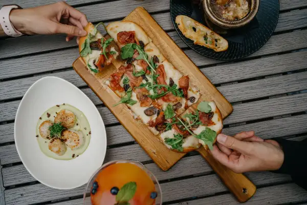Pizza wegetariańska z figami i rukolą, obok talerz z przegrzebkami i drink.