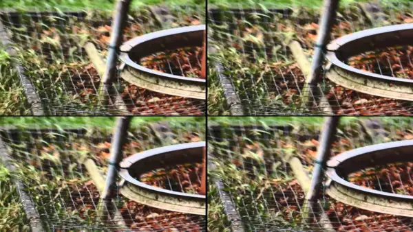 Zniekształcony obraz z efektem rolling shutter, ukazujący fragment ogrodzenia i ziemi.