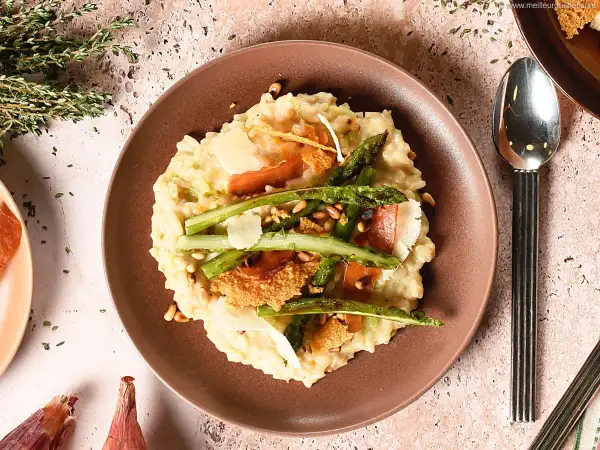 Un crémeux risotto aux asperges vertes, garni de copeaux de parmesan et de fines tranches de prosciutto. Une recette parfaite pour un repas printanier.