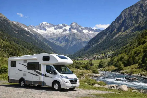 Autocaravana aparcada junto a un río en un valle alpino con picos nevados, ideal para explorar los ibones de Benasque.