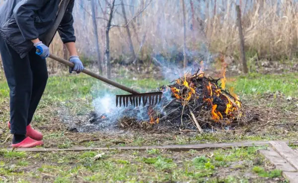 Osoba w rękawiczkach grabi ognisko na posesji, z którego unosi się dym i płomienie.