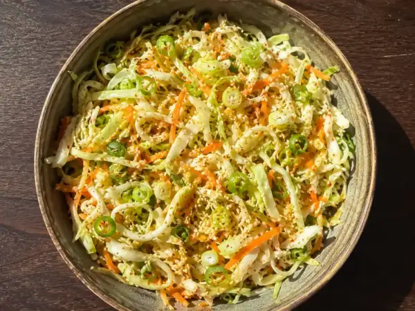 En skål med kålsallad vitkål, morötter och salladslök, toppad med sesamfrön.