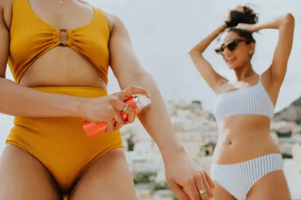 Frau trägt Sonnencreme auf, um sich vor der Sonne zu schützen. Welcher LSF ist wohl der richtige für diesen sonnigen Tag am Strand?