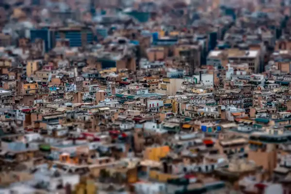 A dense cityscape rendered with tilt shift photography, making the buildings appear like miniature models.
