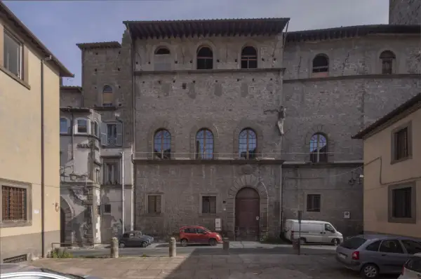 Antico palazzo chigi viterbo con finestre ad arco e un portone in legno. Auto parcheggiate nella piazza antistante.