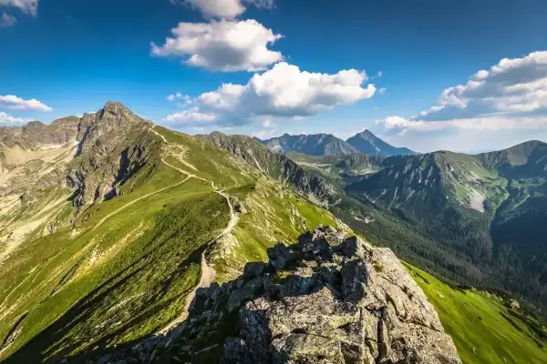 Widok na szlak prowadzący na Kasprowy Wierch. Zielone zbocza Tatr, skaliste szczyty i błękitne niebo z chmurami.