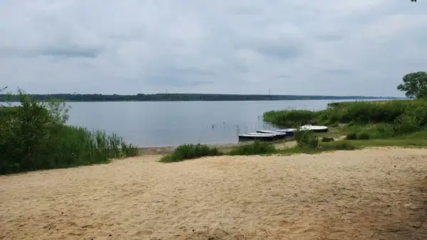 Piaszczysta plaża nad Zalewem Porajskim, z kilkoma łódkami przy brzegu. Idealne miejsce na wypoczynek i podziwianie przyrody.
