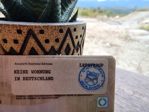 Dokument mit "Keine Wohnung in Deutschland" und einem Stempel. Ein Sukkulent in einem Topf steht daneben. So kann man dauerhaft reisend melden.