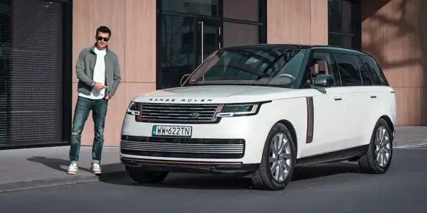 Elegancki mężczyzna w okularach stoi obok białego Range Rover 2025 z czarnym dachem.