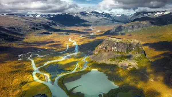 Weites Tal mit Fluss und Berg in Schwedens Nationalparks. Herbstliche Farben und dramatische Wolken über der Landschaft.