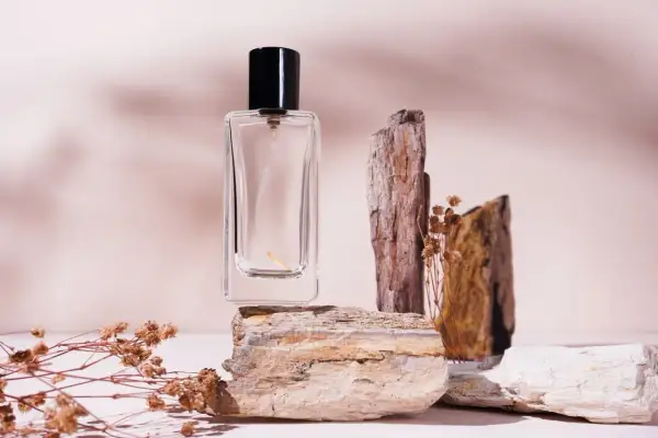 Szklana buteleczka perfum na kamieniach, otoczona suchymi gałązkami. Zapach niczym mocno pudrowe perfumy, delikatny i subtelny.