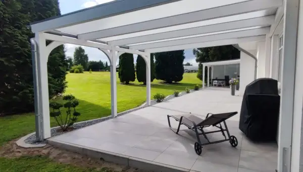 Modernes Terrassendach bauen: Ein Liegestuhl und Grill warten auf sonnige Tage unter dem neuen Dach. Der Garten lädt zum Entspannen ein.