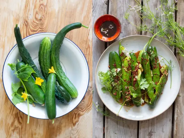 Färska gurkor i en skål och en tallrik med kryddig asiatisk gurksallad, garnerad med örter och blommor.