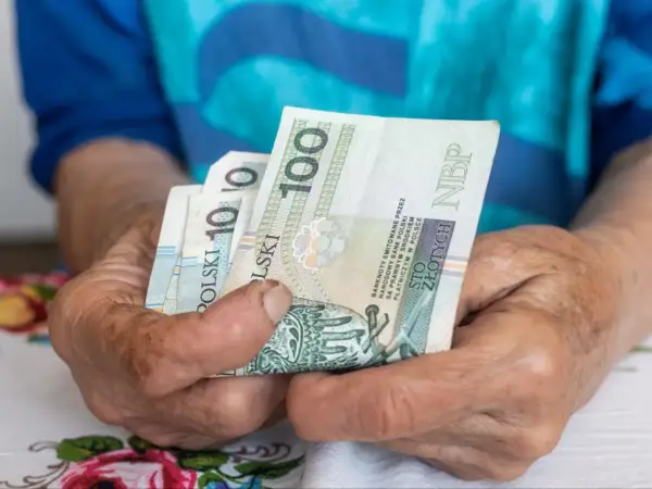 Dłonie trzymają polskie banknoty 100 zł. Czekamy na informacje, kiedy będzie wypłacana trzynastka.