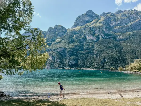 Chłopiec bawi się na plaży nad Jeziorem Garda, w tle góry. Idealne pola kempingowe czekają na odkrycie.