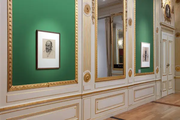 Een portret van Julie de Graag hangt aan een groene muur, naast een grote spiegel en een deur.