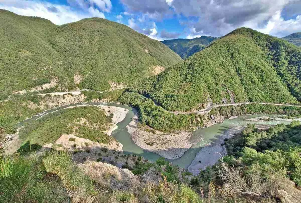 Un fiume serpeggia tra montagne verdi e scoscese, con una strada che costeggia il corso d'acqua. Il borgo di Brugnello si intravede tra la vegetazione lussureggiante.