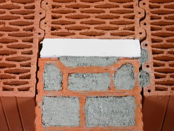 Zbliżenie na pustaki ceramiczne z zaprawą i białym elementem izolacyjnym.
