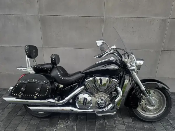 Czarny motocykl Honda VTX 1800 Neo z sakwami i oparciem dla pasażera, lśniący chromem na tle szarej ściany.