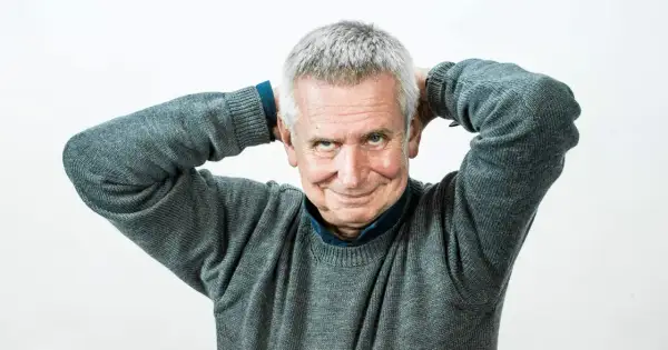 Uśmiechnięty mężczyzna z siwymi włosami, który trzyma ręce za głową. To on jest tym, kto pisze teksty żartów i anegdot, które opowiada prowadzący show.