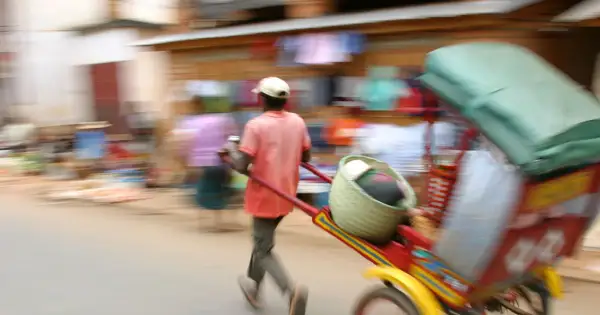 Madagaskar ludność w ruchu. Mężczyzna ciągnie wózek z koszem i towarami, pośród zamazanych postaci na targu.