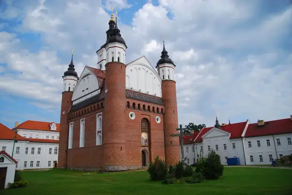 Ceglana cerkiew z kopułami i krzyżem, przypominająca o historii **unii brzeskiej**. Obok białe budynki klasztorne.