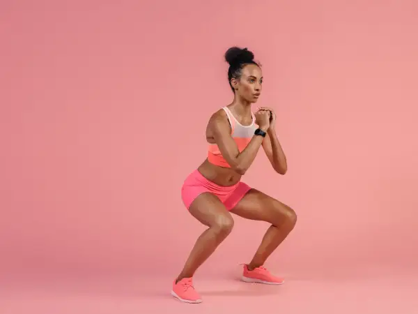 A woman in athletic wear performs pulsing squats, her hands clasped in front of her chest.