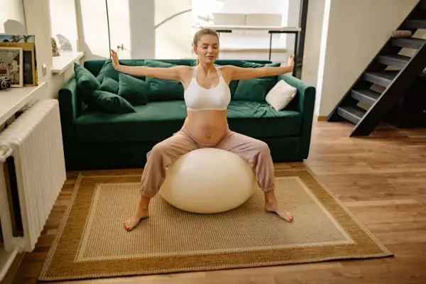 Femme enceinte faisant un exercice avec ballon pour perdre du ventre, bras écartés, yeux fermés.