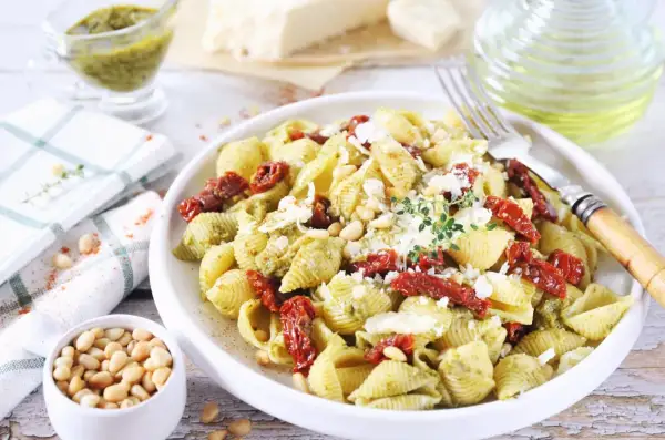 Pyszny makaron z pesto i suszonymi pomidorami, posypany parmezanem i orzeszkami pinii. Idealny na szybki obiad.