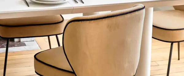 Chaises au revêtement velours couleur camel, bordées d'un passepoil noir, autour d'une table blanche.