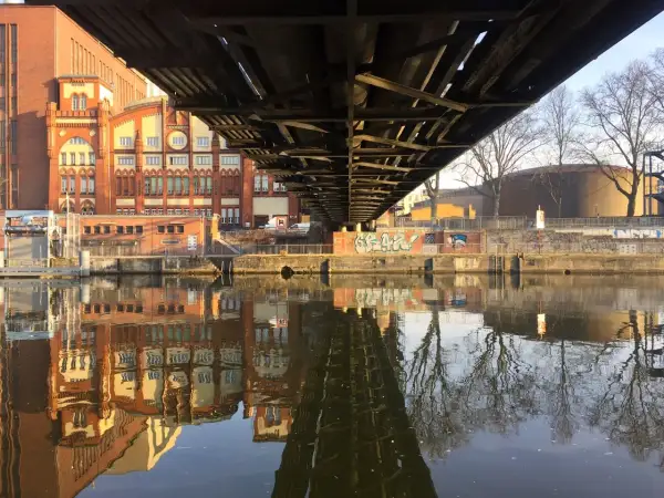 Pod mostem w Berlinie odbija się w rzece ceglana architektura i nagie drzewa.