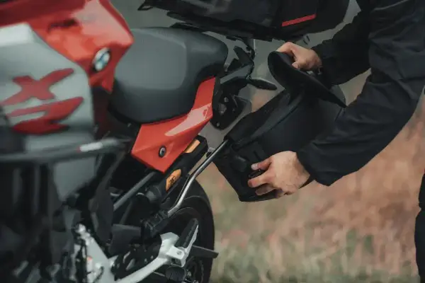 Mężczyzna montuje czarną sakwę motocyklową do czerwonego motocykla.