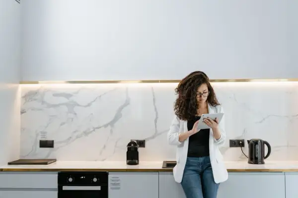 Donna con tablet in cucina moderna, valuta quanto costa rifare una cucina con finiture in marmo e illuminazione a led.