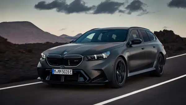 Mroczny, matowy BMW M5 Touring pędzi po pustej drodze, z górami w tle.