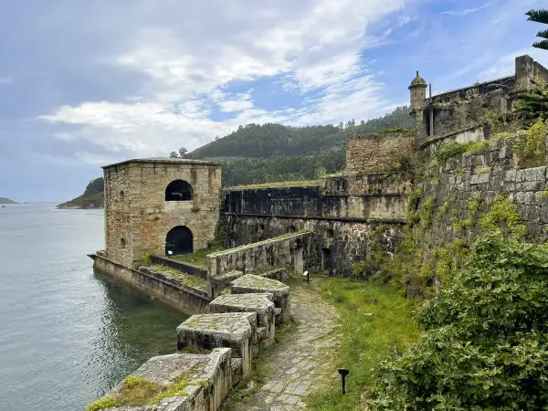 El castillo San Felipe en Ferrol, una fortaleza de piedra junto al mar, con vegetación cubriendo sus muros y un camino empedrado.
