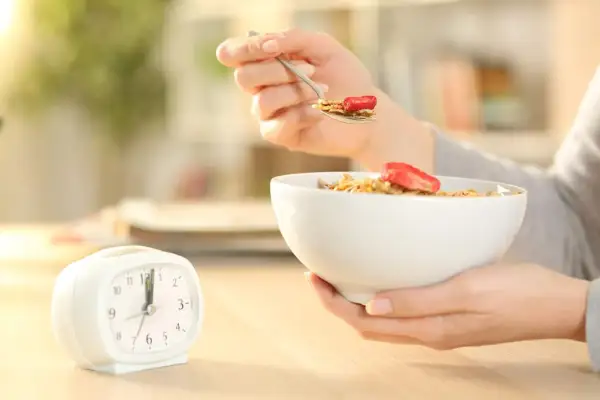 Une personne mange des céréales avec des fraises, une horloge à côté. Le jeûne intermittent avant après 1 mois, une nouvelle habitude alimentaire.