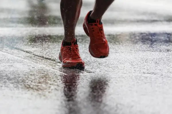 Scarpe da corsa arancioni che schizzano sull'asfalto bagnato, un'immagine di determinazione nel correre sotto la pioggia.