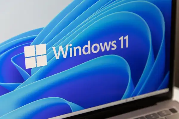 Ekran laptopa z logo Windows 11 i niebieskim, falistym tłem. System wymaga modułu TPM.