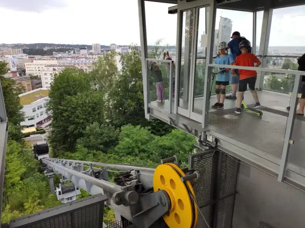 Dzieci z hulajnogami czekają na przejazd kolejką linową Gdynia. Widok na miasto i morze.