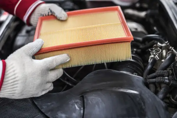 Mains gantées tenant un filtre à air propre, prêt à remplacer un filtre à air encrassé dans un moteur de voiture.