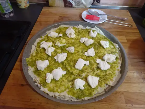 Une pizza à la pâte fine, recouverte de sauce verte et de morceaux de fromage blanc. Un délice inspiré du pain sarde.