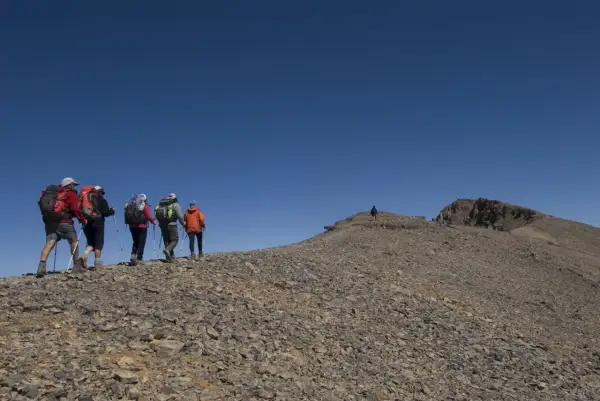 Randonneurs sur le flanc rocailleux du mont M'goun, sous un ciel bleu intense.