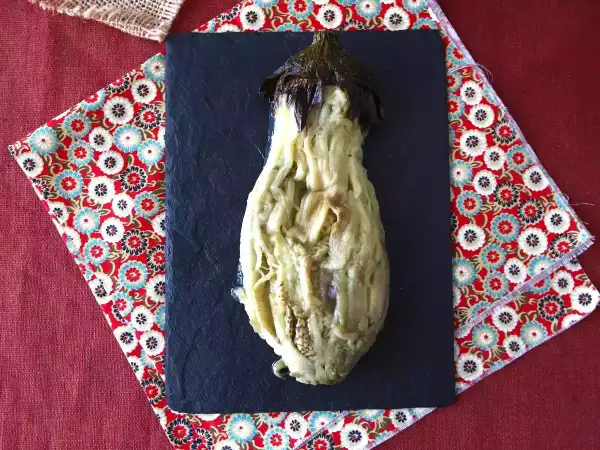 En ugnsbakad aubergine, mjuk och saftig, serveras på en svart skifferplatta.