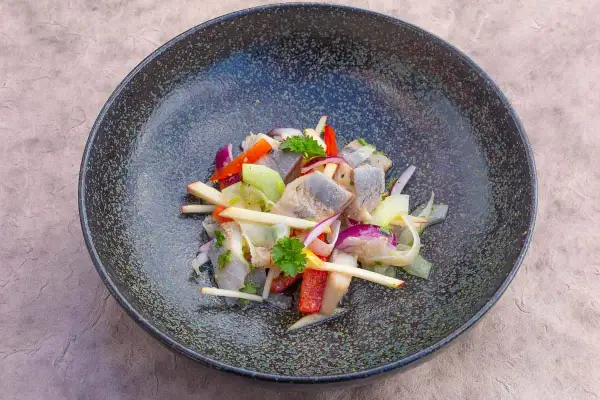 Heringssalat Hausfrauenart: ein deftiger Salat mit Hering, Apfel, Zwiebeln und Paprika in einer dunklen Schüssel.