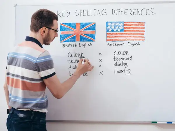 Profesor explica las diferencias de ortografía entre los tipos de inglés: británico y americano, con ejemplos escritos en la pizarra.