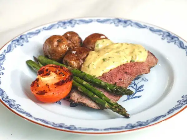 En tallrik med ryggbiff, potatis, sparris och tomat. En krämig sås toppar köttet. Ett perfekt ryggbiff recept!