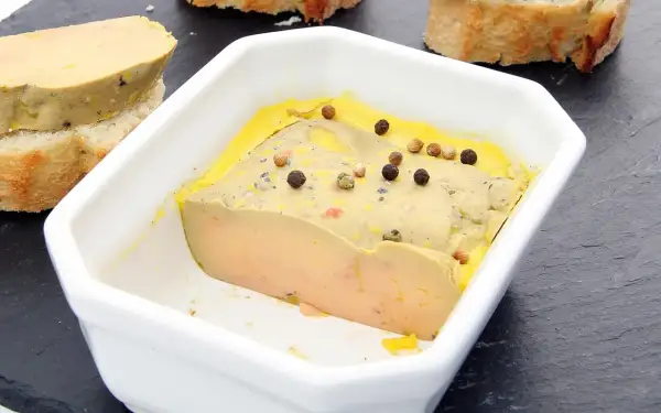 Un foie gras mi-cuit, à la texture parfaite, est servi dans un plat blanc, parsemé de grains de poivre. La température idéale pour savourer ce délice.