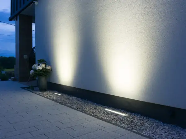 Eleganckie oprawy najazdowe subtelnie oświetlają ścieżkę i białą elewację domu, tworząc nastrojową atmosferę wieczorem.