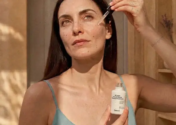 Kobieta aplikuje serum z niacynamidem i witaminą C na skórę. Produkt w białej buteleczce z pipetą.